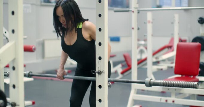 Middle aged Caucasian woman during back muscles workout barbell while standing in a tilt. With precise form, the middle-aged woman executes barbell rows in a tilted stance to build back strength.