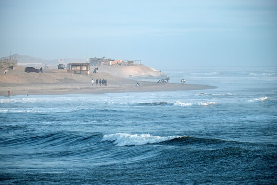 People enjoying the sunny day with clear waves rolling onto the sand at pimentel beach, peru. Coastal landscape