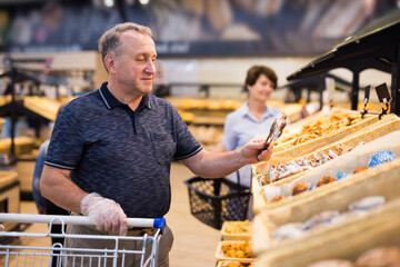 mature man choosing bread and baking in grocery section of supermarket