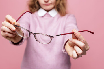 Hands holding broken eyeglasses with separated temple arm close up on pink background