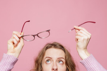 Woman holding snapped eyeglasses and detached arm with copy space on pink background