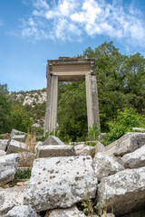 The ruins of Hadrian Gate in the ancient city of Termessos, framed by trees and a rocky foreground