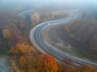 Aerial view of a single car driving on a winding foggy mountain road at sunrise