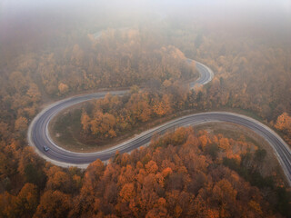 Aerial view of a single car driving on a winding foggy mountain road at sunrise