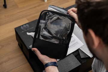 Person's hands carefully holding a black transparent-window zippered pouch containing electronic accessories, emphasizing organized product unboxing and setup