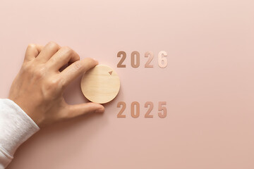 A hand places a wooden disc for the year 2026, changing from 2025, symbolizing the transition to a new year.