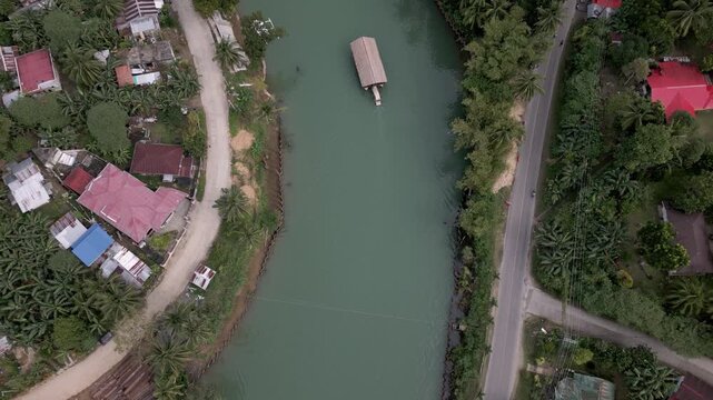 Aerial drone rise revealing Loboc River with boat navigating through tropical village. Aerial drone footage rising vertically to reveal the Loboc River in Bohol, Philippines, with a boat sailing throu