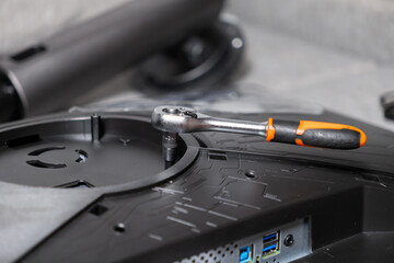 Silver ratchet wrench with orange handle resting on black electronic monitor panel, representing technology assembly, repair, and DIY hardware maintenance work