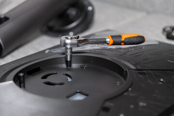 Close-up of a silver ratchet wrench with orange and black handle tightening a screw on a complex disassembled electronic device, highlighting precision repair work