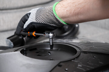 Technician's gloved hand precisely using a ratchet wrench to fasten a screw on a black monitor stand, symbolizing careful assembly and technology repair service