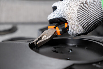 Skilled professional's gloved hand expertly uses orange-handled pliers to adjust a tiny component on a sleek black electronic device, highlighting detailed technical assembly or repair work