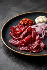Macro Shot of Traditional Halal Balkan Dry Meat Platter with Sudzuk, Dry Beef Salami and Basturma on Matte Black Surface