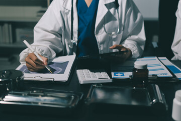 Two doctors and a female nurse meet at a table in the hospital, collaborating on medical tasks using laptops and computers