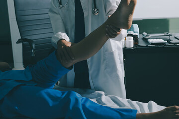 Doctor examining and supporting injured ankle of female patient in hospital room, providing medical assistance and treatment for sprain or fracture