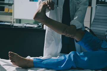 Doctor examining and supporting injured ankle of female patient in hospital room, providing medical assistance and treatment for sprain or fracture