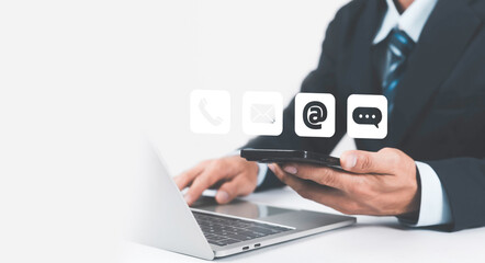 Businessman using smartphone and laptop for digital communication, online contact, customer support, and business technology concept with email, phone, and chat icons on virtual interface.