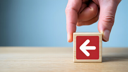 Hand placing wooden block with left arrow symbol on a wooden surface, representing direction and decision-making