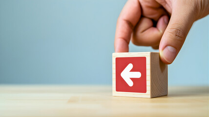 Hand arranging wooden cube block with an arrow symbol, signifying the concept of navigating back, making a critical decision, or changing direction in business strategy or personal development