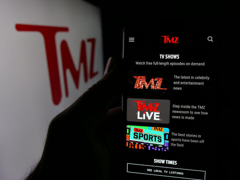 Stuttgart, Germany - 12-12-2025: Person holding smartphone with web page of US tabloid news company TMZ on screen in front of logo. Focus on center of phone display.