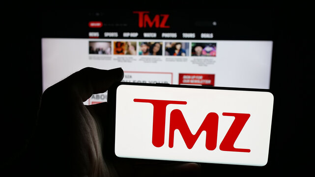 Stuttgart, Germany - 12-12-2025: Person holding mobile phone with logo of US tabloid news company TMZ on screen in front of web page. Focus on phone display.
