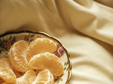 Peeled mandarin segments in decorative bowl on soft fabric background