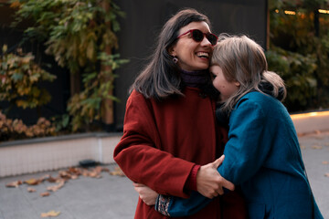 Happy mother and daughter wearing coats having fun together at walk in city at autumn evening