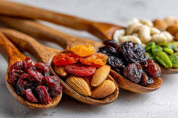 Assorted nuts and dried fruits arranged in small piles with wooden scoop on white surface