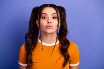 Young female teen model with playful kiss pose in orange shirt against purple background