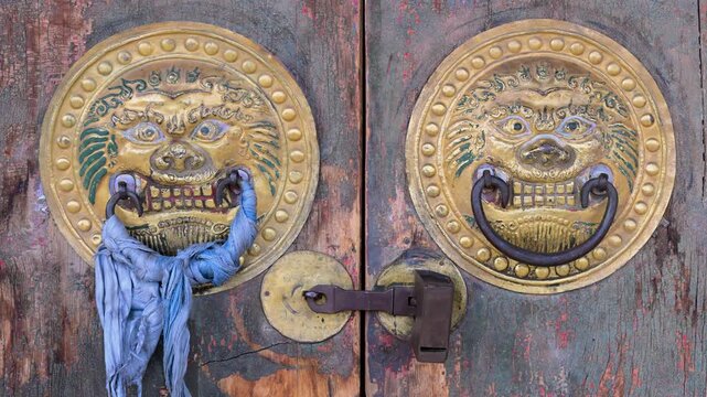 Close up of an antique wooden door with golden lion-head knockers at Erdene Zuu Monastery in Kharkhorin, Mongolia. Weathered texture and traditional Buddhist art.