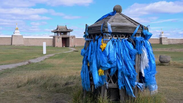 Blue prayer ribbons (Khadag) tied to a wooden shrine at Erdene Zuu Monastery in Kharkhorin, Mongolia. Buddhist spiritual offerings with the historic gate in the background.