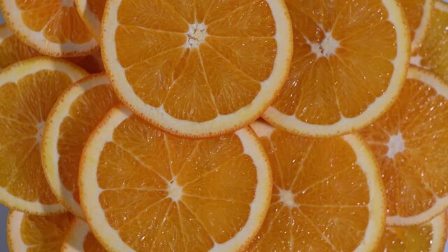Seamless loop video clip shot from directly above. Fresh orange slices are arranged in a circular pattern on a dark turntable, rotating in a smooth, continuous motion. This clip creates a mesmerizing,