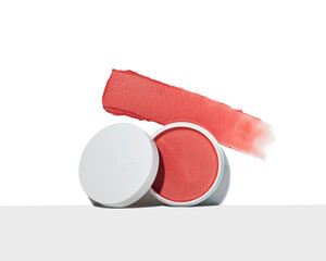 Vibrant coral cream blush pot featuring a textured swatch smear against a clean white background in a studio shot.
