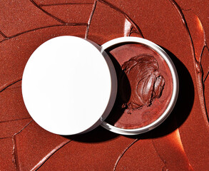 Overhead closeup view of richly pigmented terracotta bronze makeup balm product displayed open on a textured shimmering background