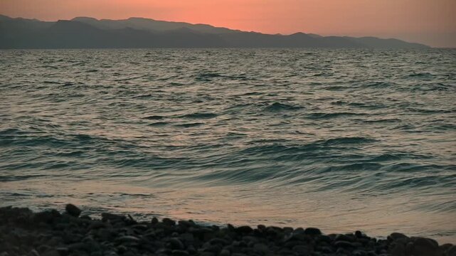 Breathtaking panoramic shot of a vivid Mediterranean sunset on the coast of Cyprus. The camera captures the sun dipping below the horizon, painting the sky in shades of orange, pink, and purple. 