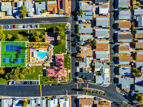 High altitude aerial view of suburban residential neighborhoods in Los Angeles, California, showing dense housing blocks, wide roads, undeveloped land, and distant mountains under clear blue sky