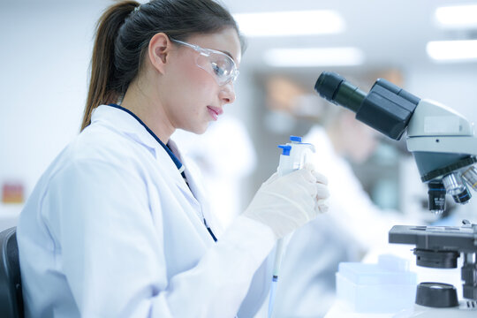 Focused female pathologist using a microscope to examine tissue biopsy samples in a sterile hospital laboratory. Professional scientist conducting medical research for disease diagnosis.