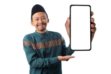Excited Indonesian Muslim man in a green koko shirt and black peci called songkok presenting a phone with a blank white screen toward the camera, isolated on a white background