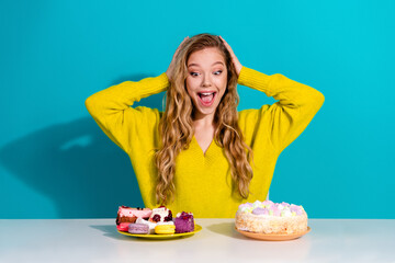Young woman in bright yellow sweater excited by dessert plate with cake and macarons against blue...