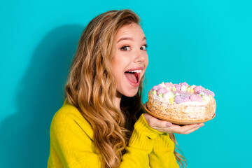Young woman holding a cake with colorful frosting and smiling against a bright blue background