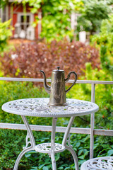 Metal teapot sits on small white table in garden