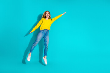 Young woman jumping in bright yellow sweater against blue background for lifestyle fashion...