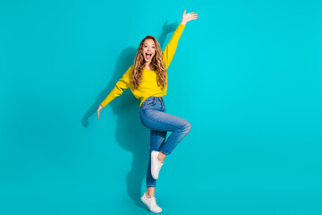Young woman jumping with joy wearing a yellow sweater jeans and white sneakers against a bright...
