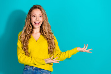 Young woman in a yellow sweater gestures with open hands against a blue background smiling for lifestyle advertising