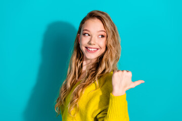 Young woman in a bright yellow sweater smiles and points to the right against a vivid blue...