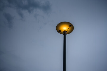 Single street lamp illuminated at twilight against a soft blue sky. Minimal urban scene expressing calm, solitude, safety and guidance. Ideal for concepts of night, energy, city life and copy space