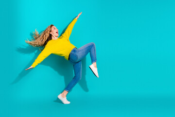 Young woman in yellow sweater jumps against blue background for vibrant lifestyle advertising