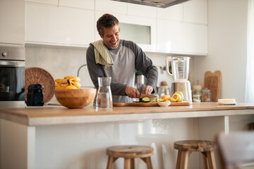 Happy Man Chopping Vegetables in Modern Kitchen With Blender and Fresh Fruit