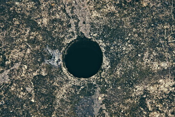 Deep circular hole in a weathered concrete and mossy surface. Conceptual image of a void, pit, or...