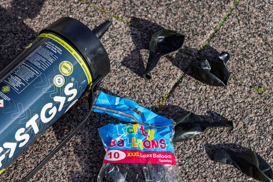 Discarded nitrous oxide cylinder and empty balloons lying on pavement, representing recreational drug use litter and environmental waste.