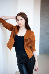 Professional fashion model wearing brown jacket and black outfit posing in studio on clean background, elegant young woman portrait for modeling agency portfolio, modern commercial beauty photography